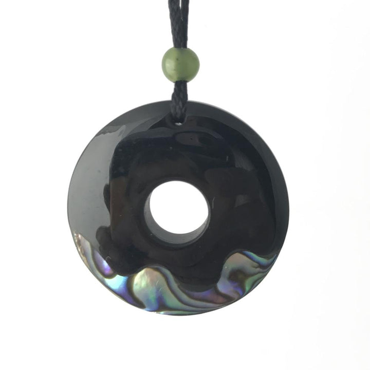 Donut shaped black pendant with a central hole on a cord, accented by a green bead above
