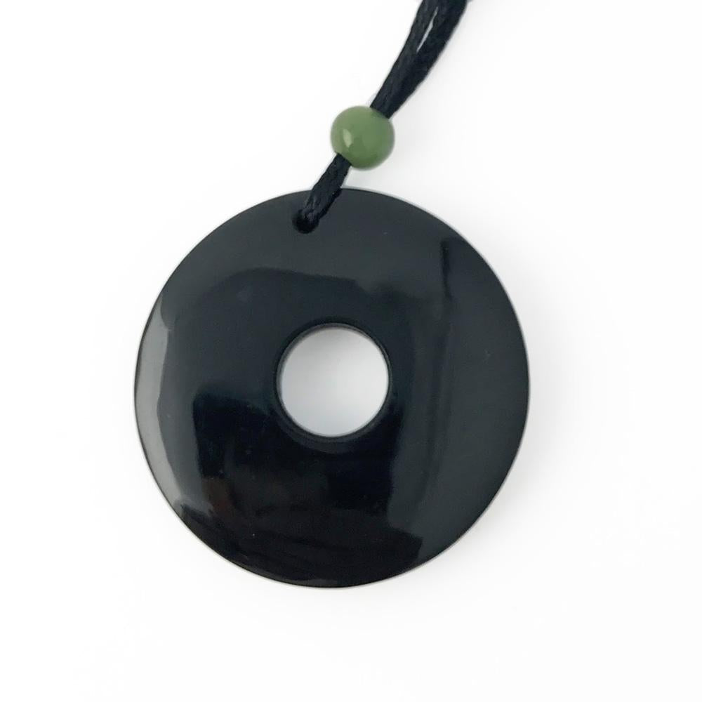 Black circular donut pendant with central hole on a black cord and a small green bead.