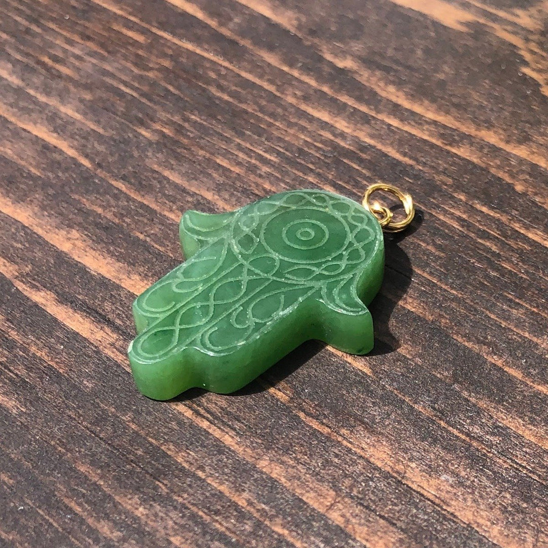 Close-up of green carved Hamsa hand pendant with circular center and looping patterns on a wood surface