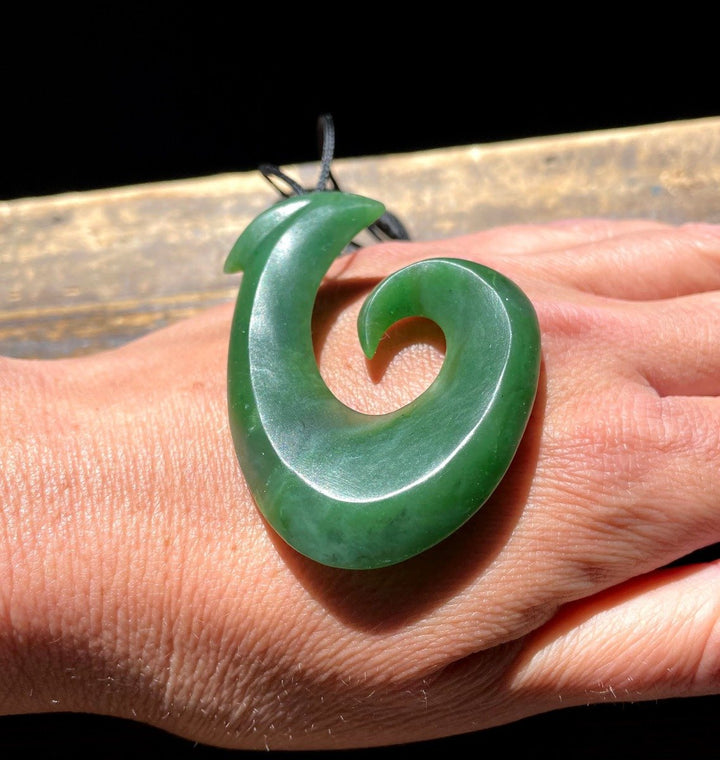 Close-up of a large green jade fish hook pendant resting on a person&