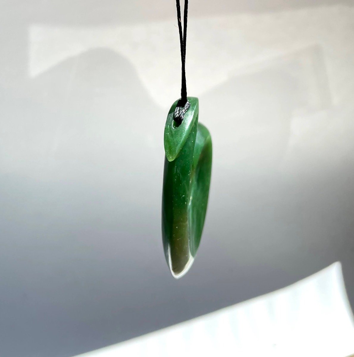 Large 59mm jade fish hook pendant in vibrant green with lighter tip, strung on a black cord