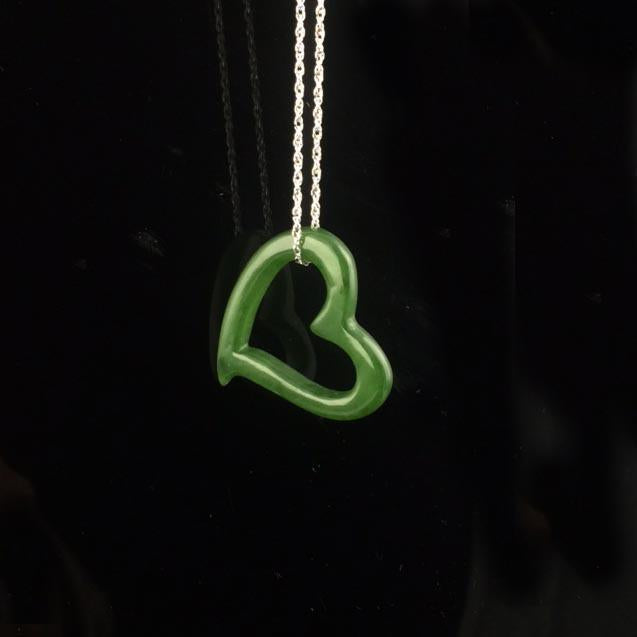 Emerald green heart shaped pendant on a silver chain against a black background.
