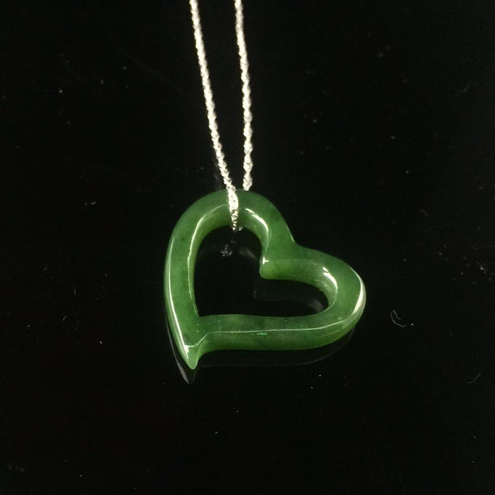 Green heart shaped pendant on a silver chain against a black background.