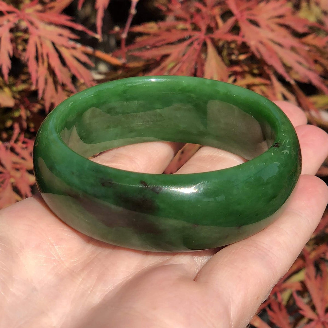 AA Bangle 50 x 18mm in green jade held in hand with red foliage in background.