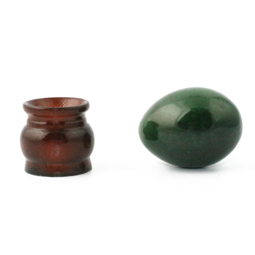 Small brown ceramic jar beside a glossy dark green egg on a white background.