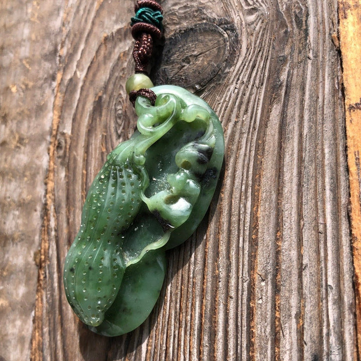Green jade peanut pendant on brown braided cord necklace against rustic wooden background.