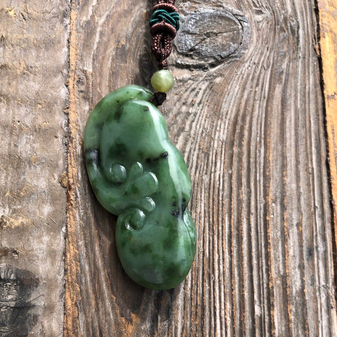 Green jade peanut pendant on brown cord with bead, photographed from the side on rustic wood