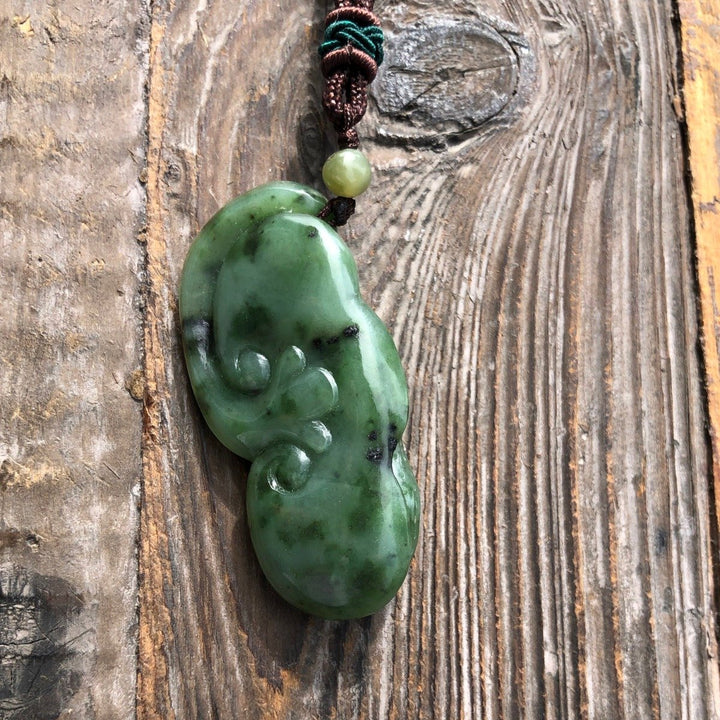 Green jade peanut pendant on brown cord with bead, photographed from the side on rustic wood