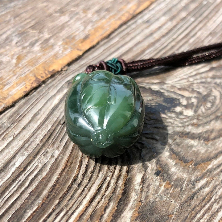 35mm green jade squash pendant on a brown cord laid on weathered wood.