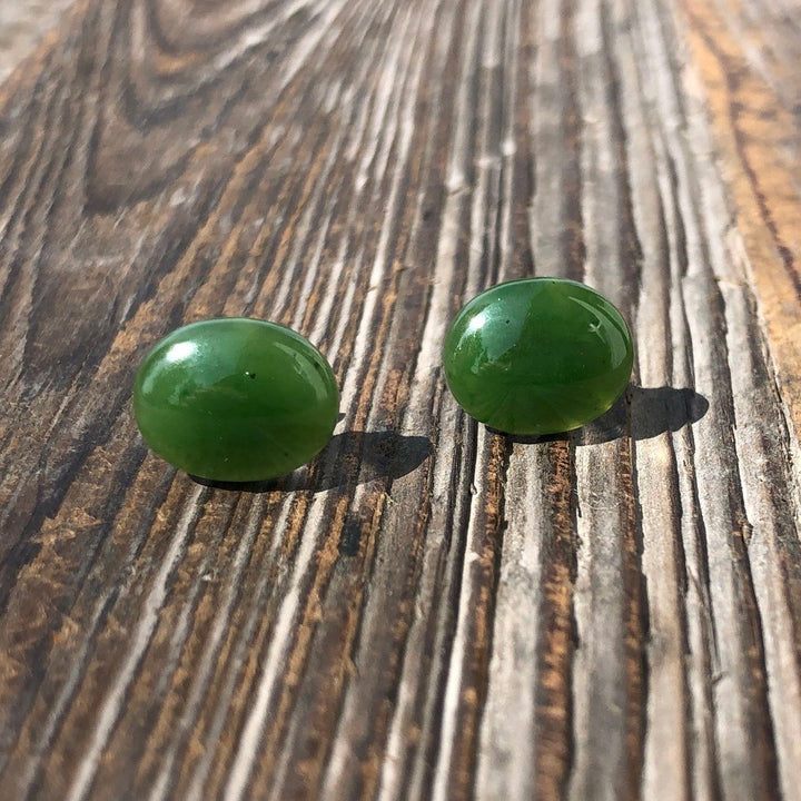 Two green oval stud earrings in two sizes on a rustic wooden surface