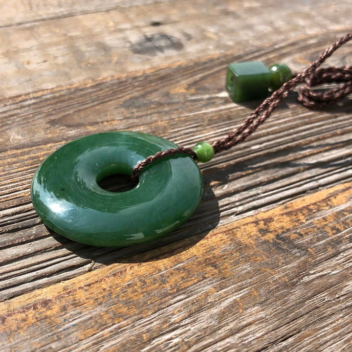 Close-up of jade donut pendant with cord and bead on rustic wooden surface