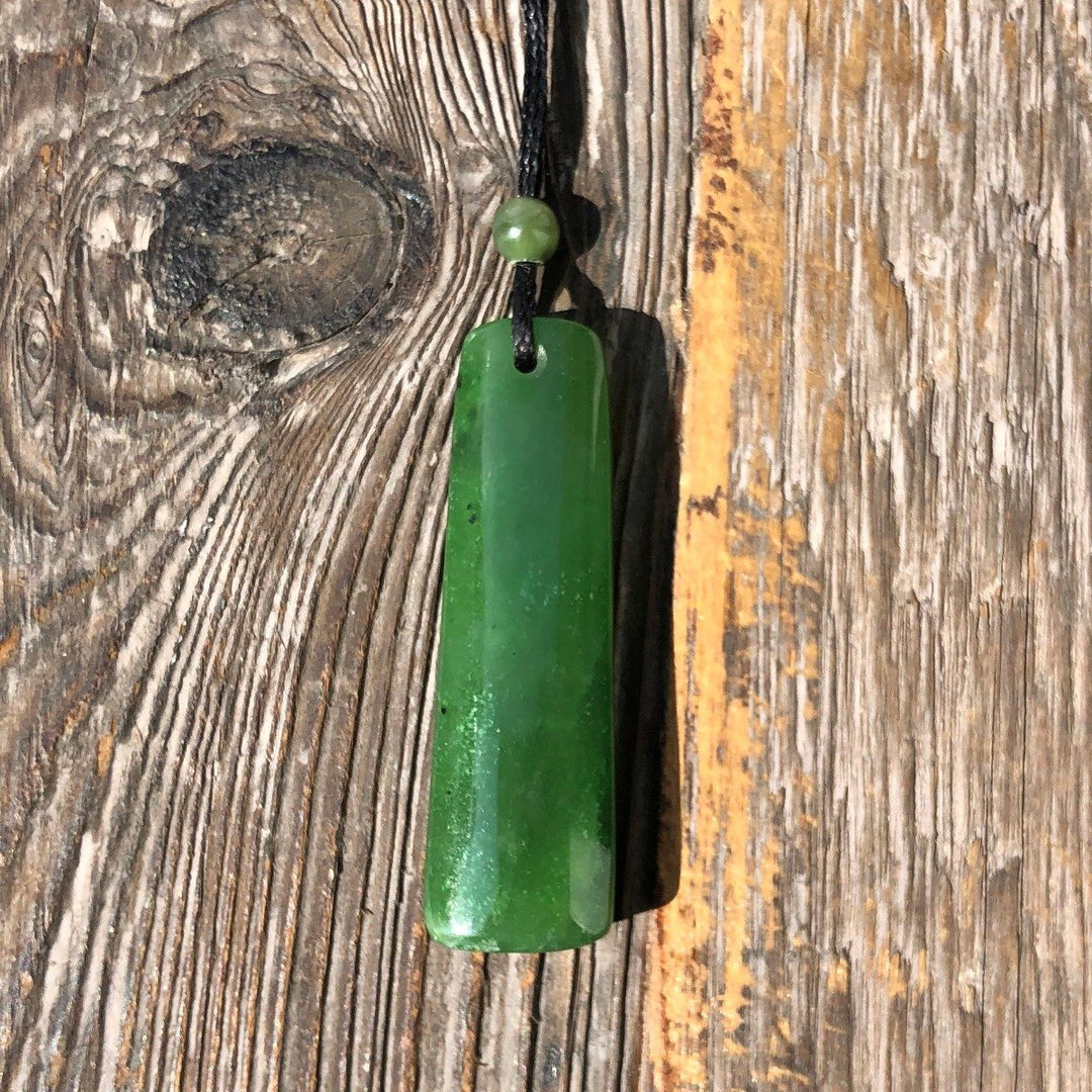 Green cylindrical jade pendant on a black cord with a small green bead