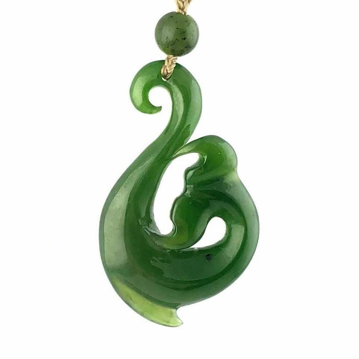 Green jade pendant with a stylized curved swirl design suspended on a beige cord with a round bead