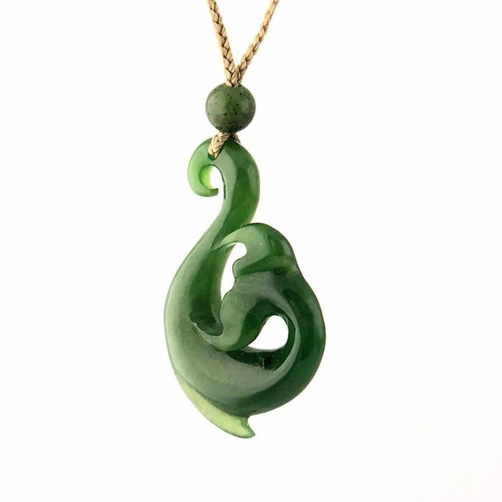 Green jade pendant shaped into a flowing swirl with a round bead above, hanging on a tan cord.
