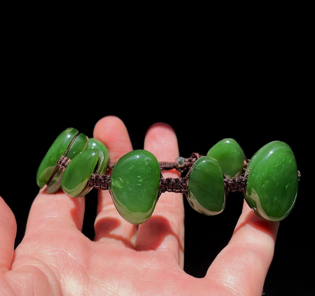 Bracelet with large green oval beads strung on braided cord against a black background.