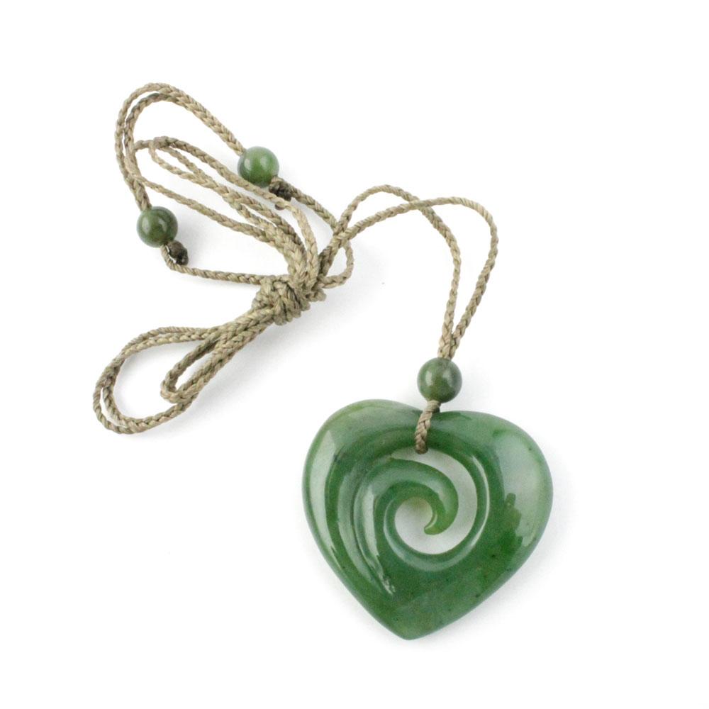 Jade pendant in a swirling koru heart shape hanging from a braided beige cord with green beads