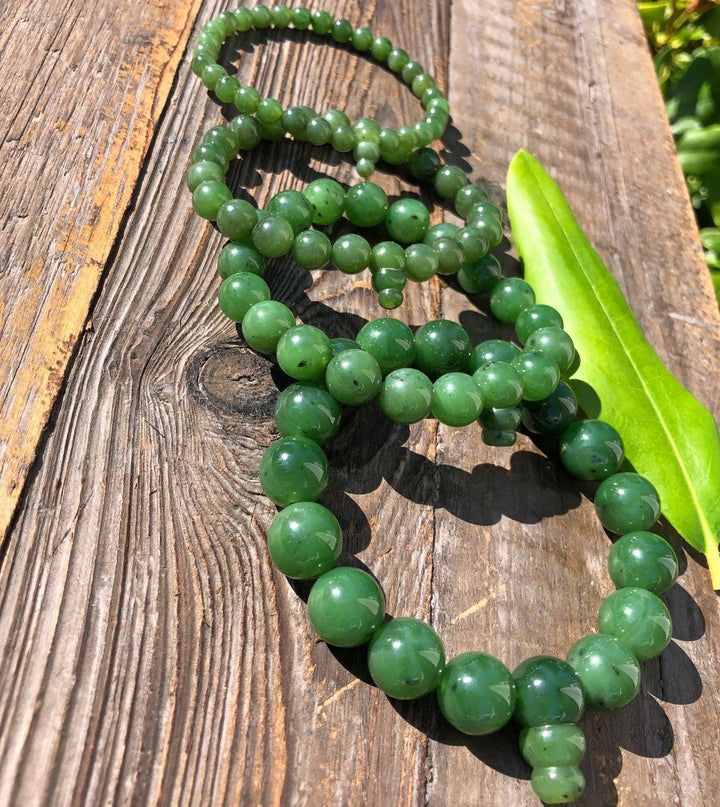 Green jade mala bead strands draped over weathered wood with a leaf.