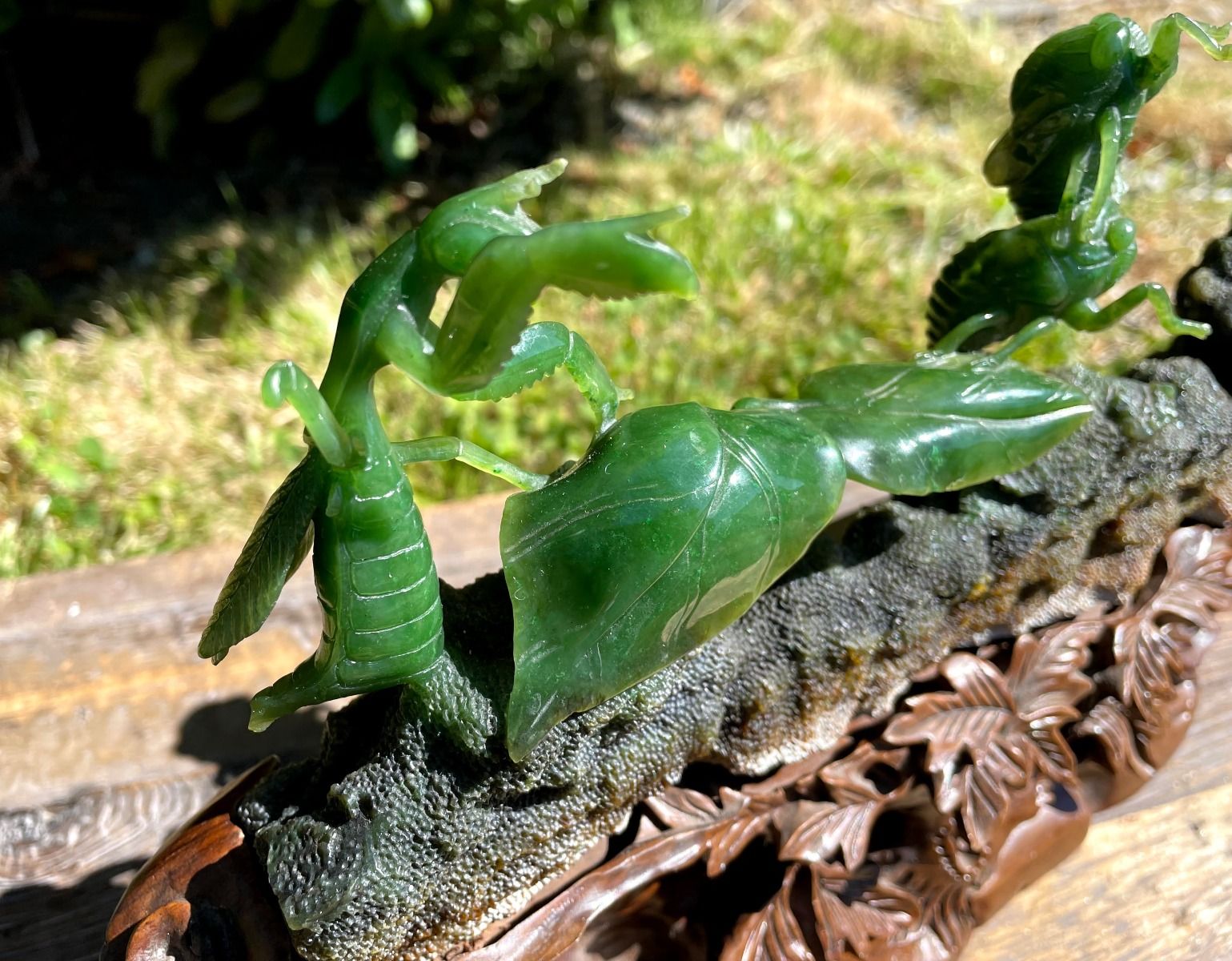 Close up of a green jade praying mantis carving on a rough dark rock base with carved leaf details