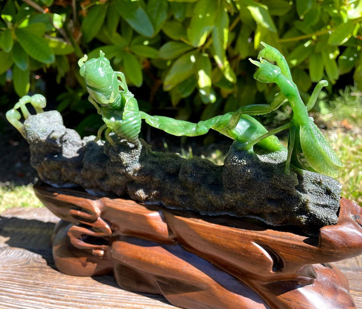 Jade praying mantis carving showing two green mantises on a rugged rock base set in a carved wooden stand