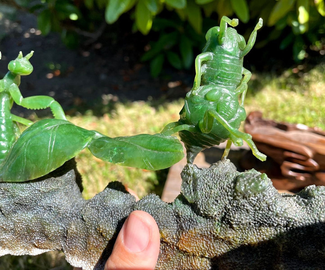 Green jade praying mantis carving with two mantises perched on a rough rock base mounted on a wooden stand