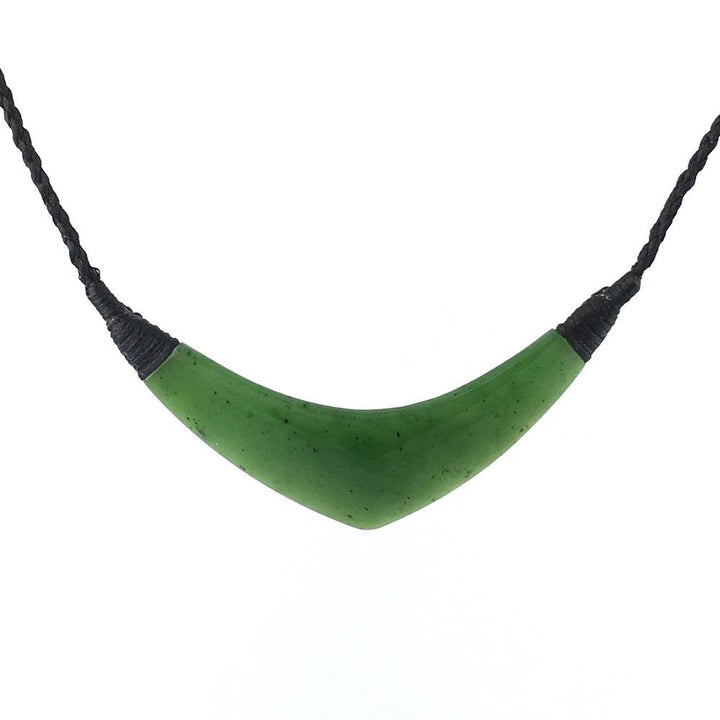 Close-up of a crescent shaped jade pendant in rich green on a black braided cord against a white background.
