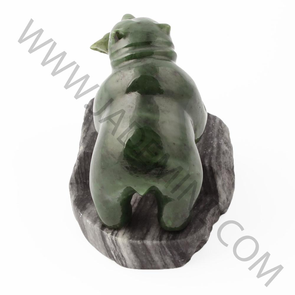 Rear view of green bear statue on a dark granite base.