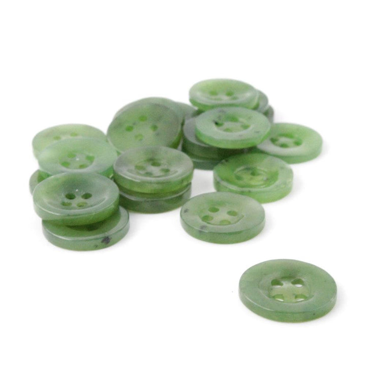 Close up of green four hole buttons scattered on a white surface