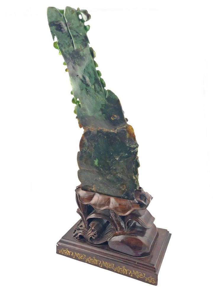 Jade dragon sculpture viewed from the side on a decorative carved wooden pedestal.
