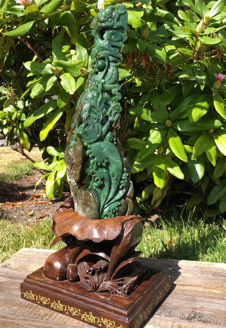 Jade dragon statue outdoors on a carved wooden pedestal beside green shrubbery