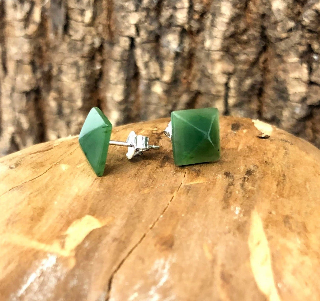 Two green jade square pyramid earrings with silver posts and butterfly backs on a wooden surface.