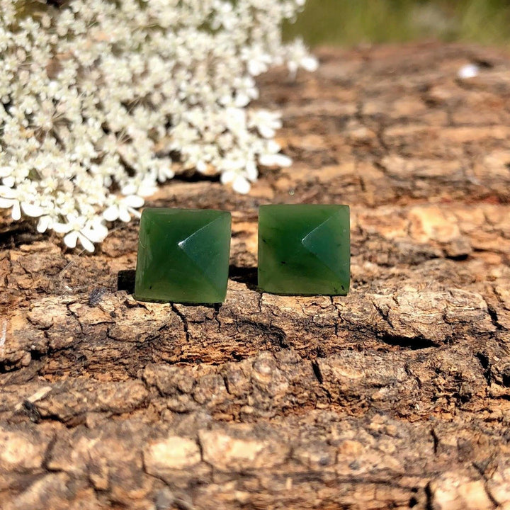 Pair of green jade square pyramid earrings 15mm with posts on rugged tree bark background.