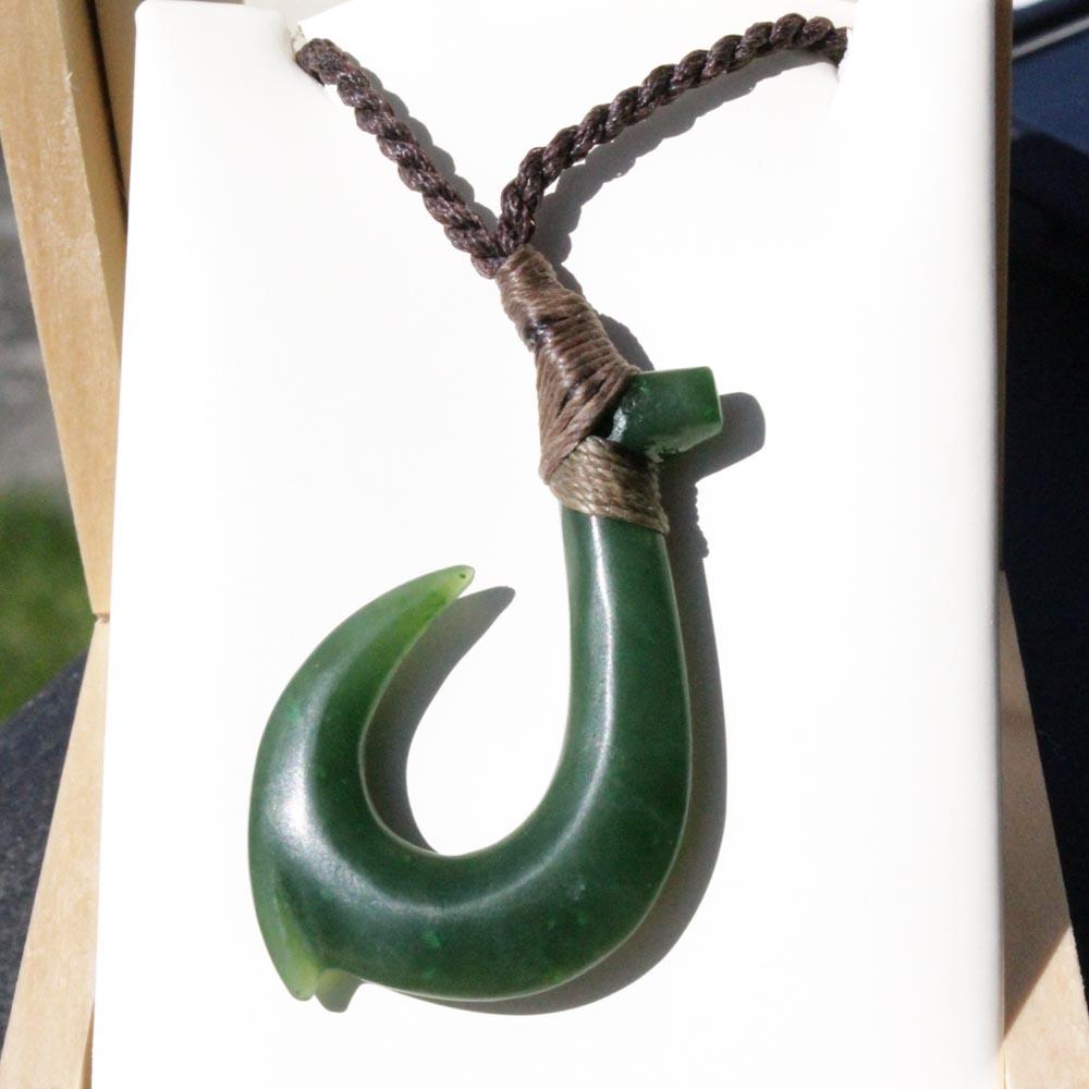 Close up of jade fish hook pendant with wrapped cord against white background.