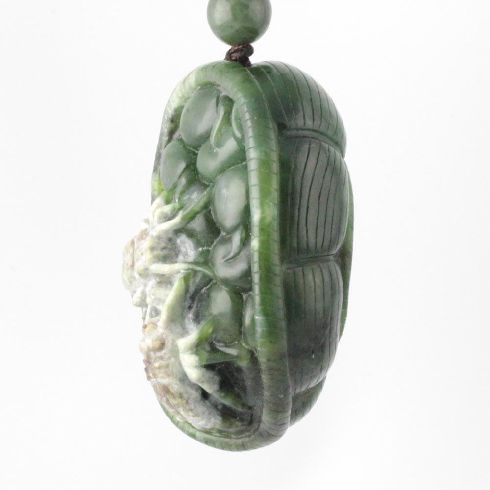 Green jade oval pendant carved with a spider motif suspended from a cord with a small bead above