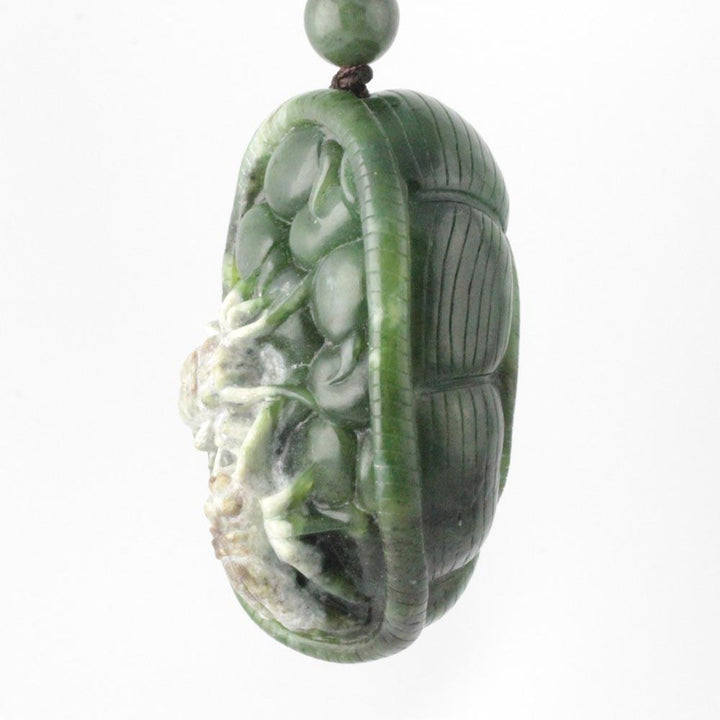 Green jade oval pendant carved with a spider motif suspended from a cord with a small bead above