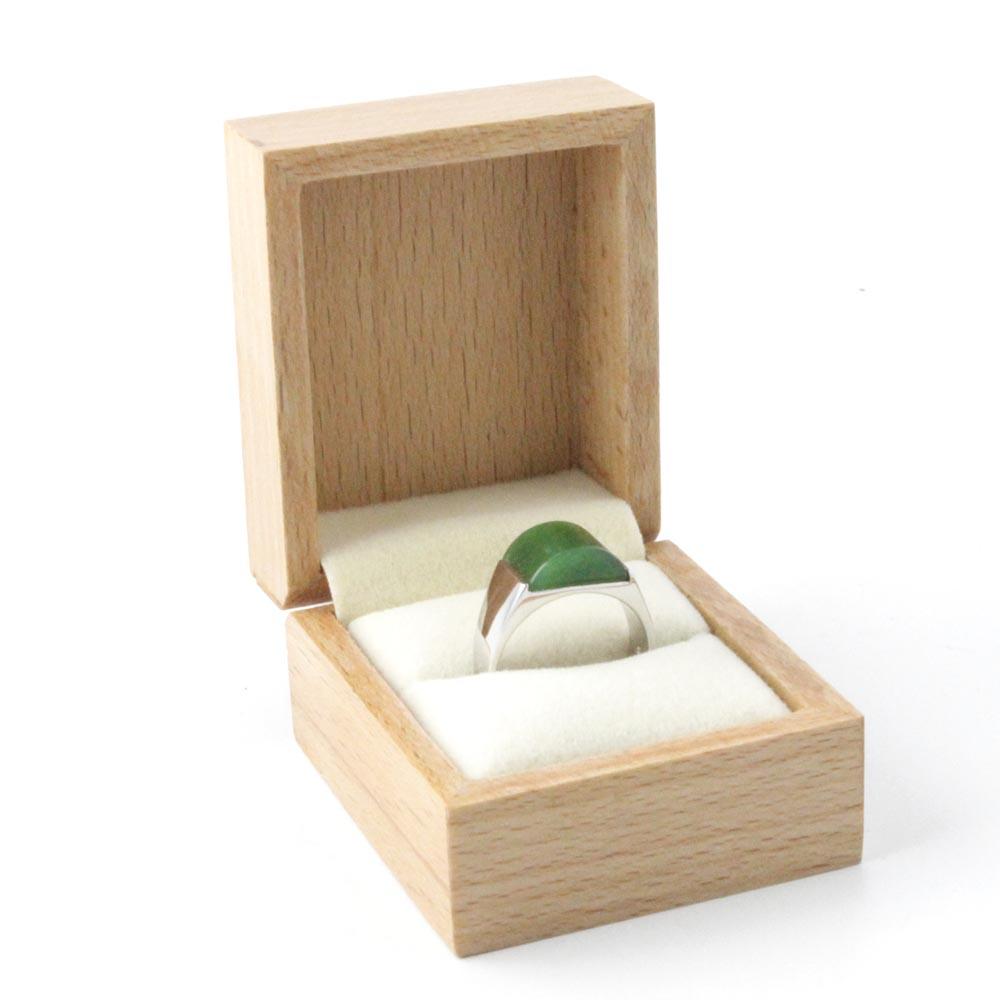 Green jade ring set in a silver band inside an open wooden jewelry box with white cushion