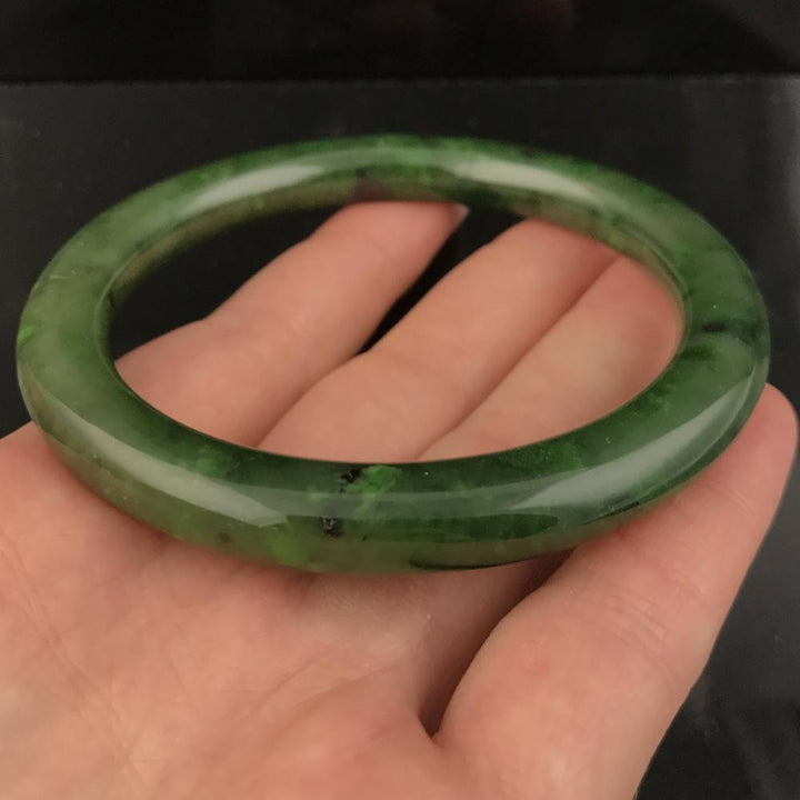 Canadian jade round bangle resting on fingers against a dark background