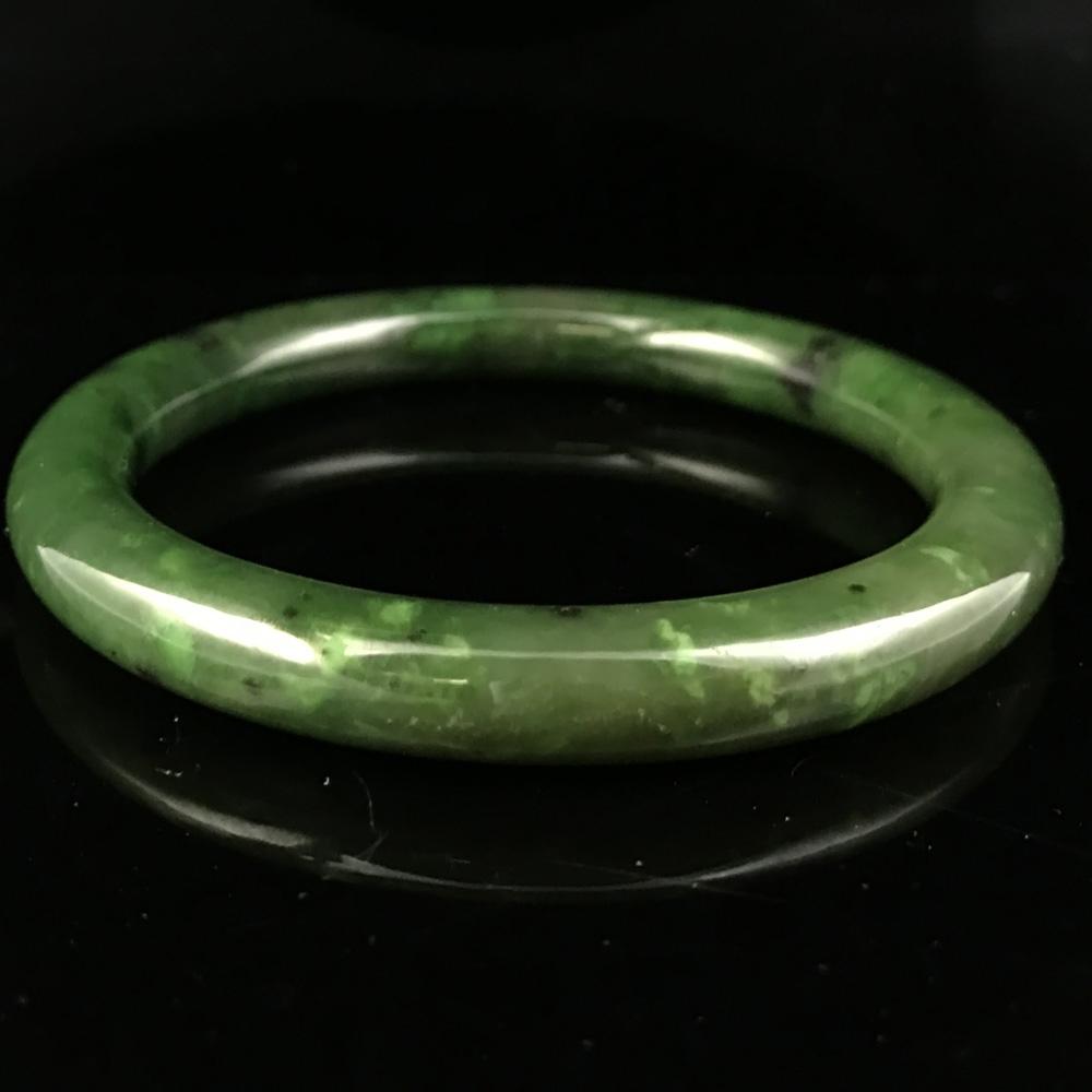 Canadian jade round bangle displayed on a black reflective surface