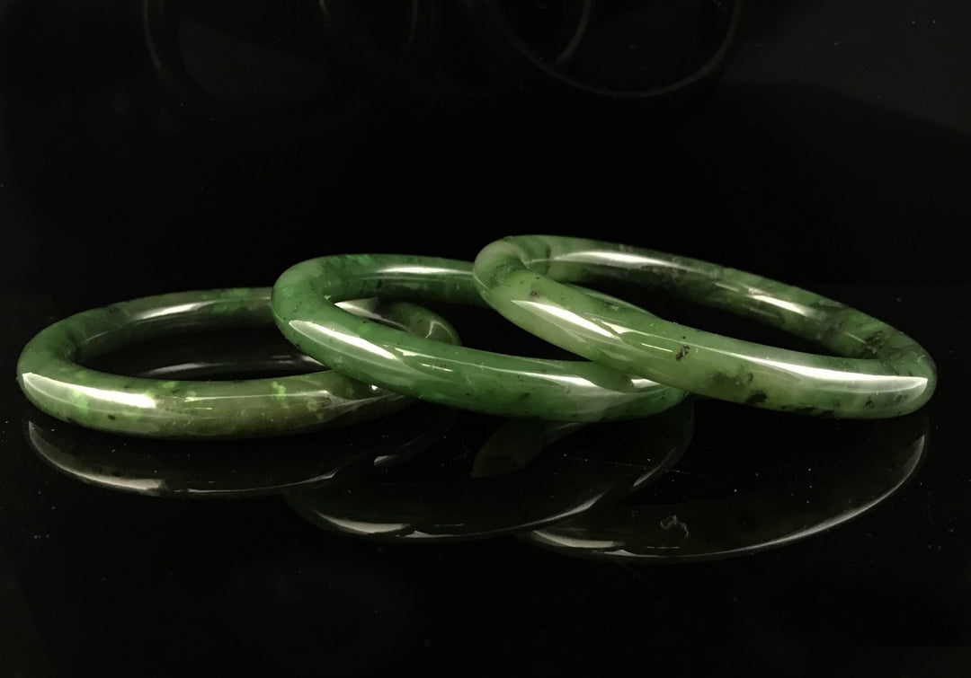 Three polished green jade bangles stacked on a black reflective surface