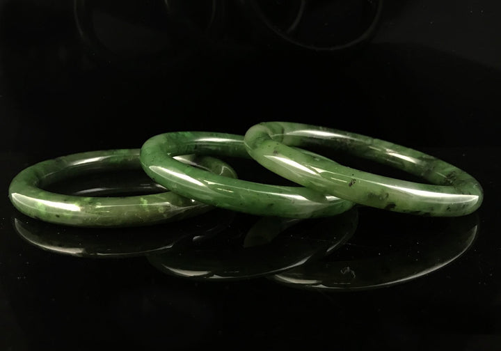 Three polished green jade bangles stacked on a black reflective surface
