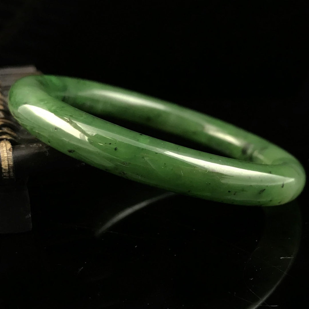 Close-up of a polished green jade bangle with natural dark inclusions