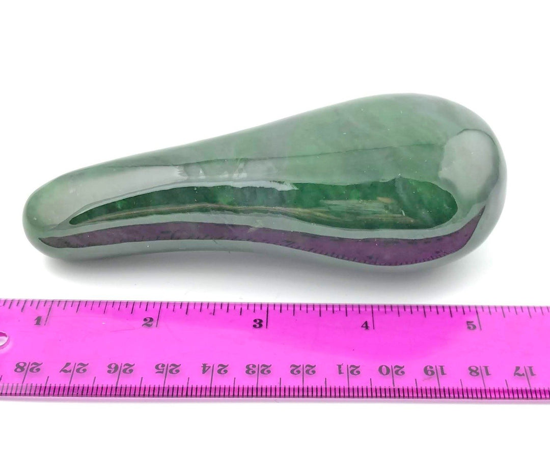 Solid green Canadian jade massage tool with a purple edge on a white background beside a pink ruler