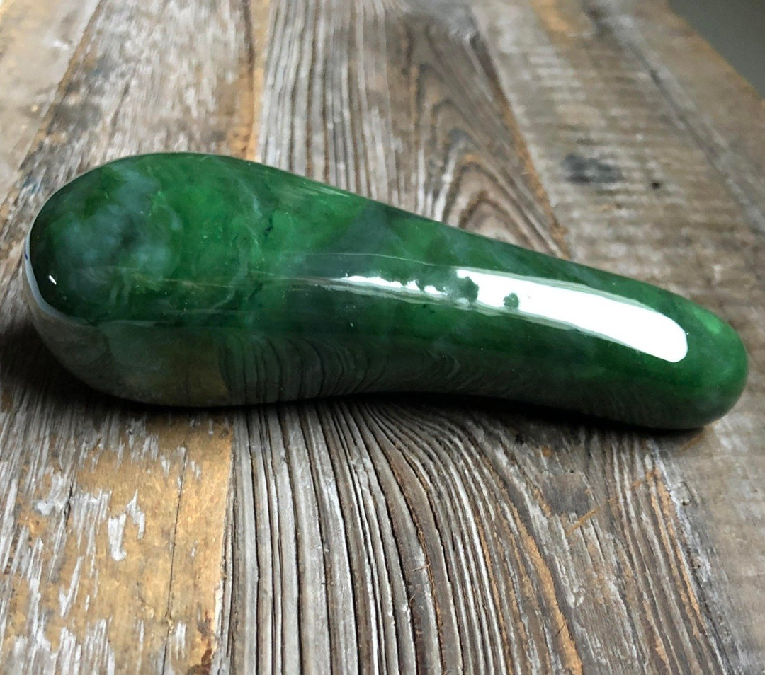 Green jade facial roller with dual ends and gold hardware resting on a rustic wooden surface
