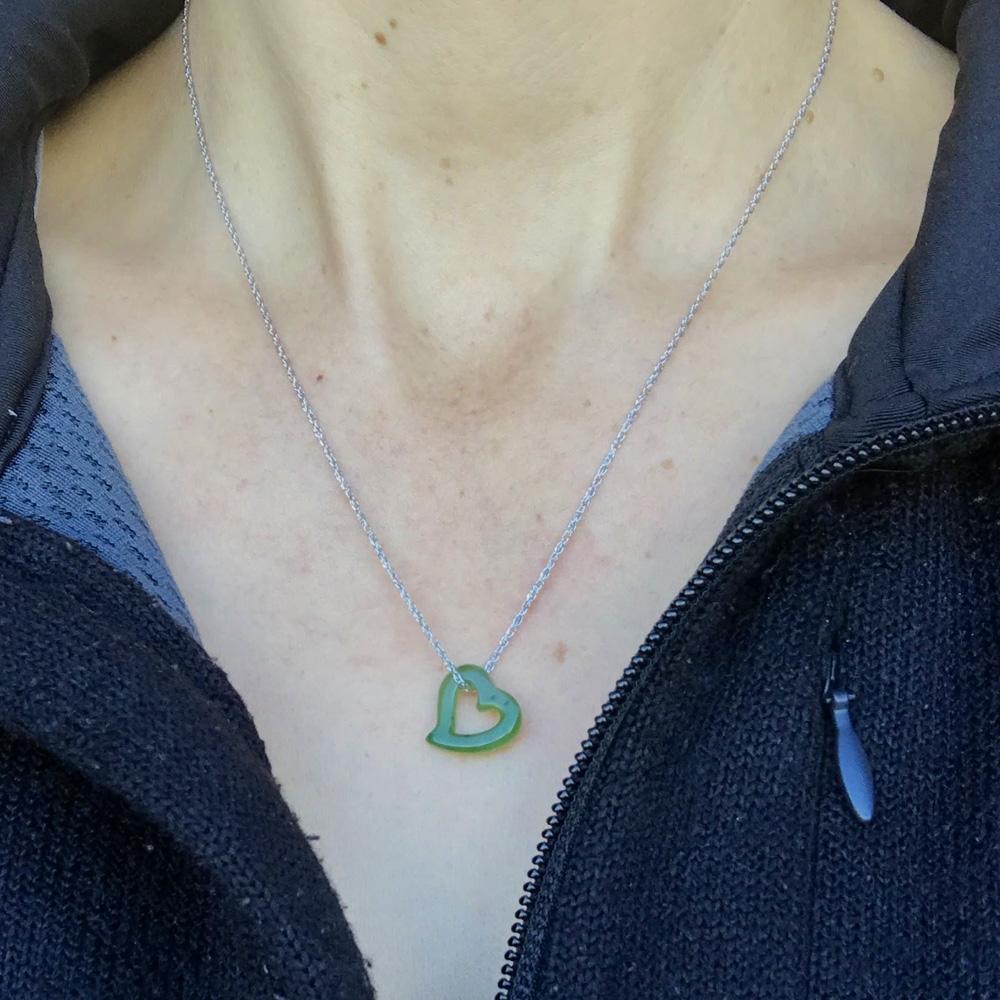 Floating jade heart pendant necklace worn on a silver chain at the neckline