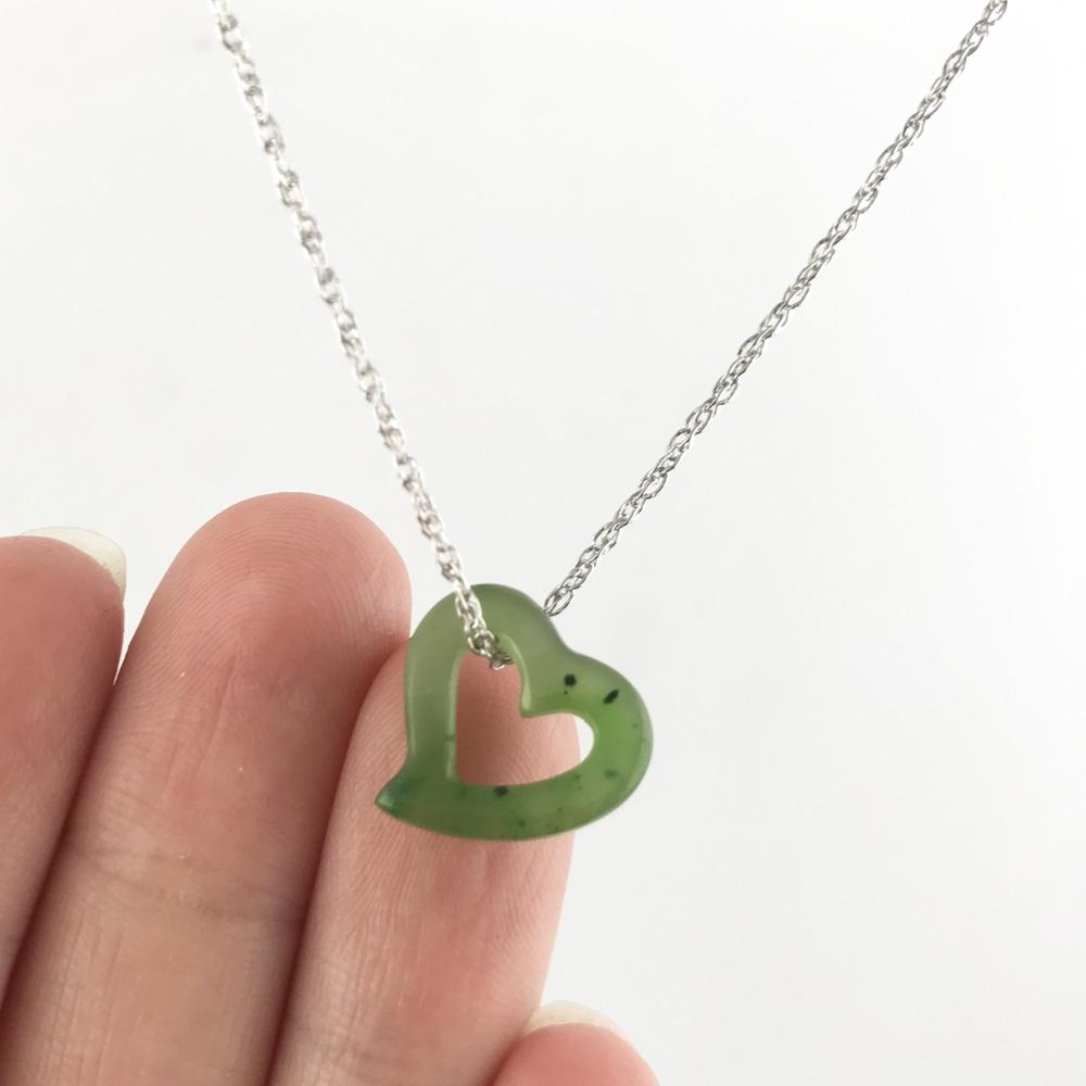 Green jade heart pendant with a hollow center held between fingers on a silver chain
