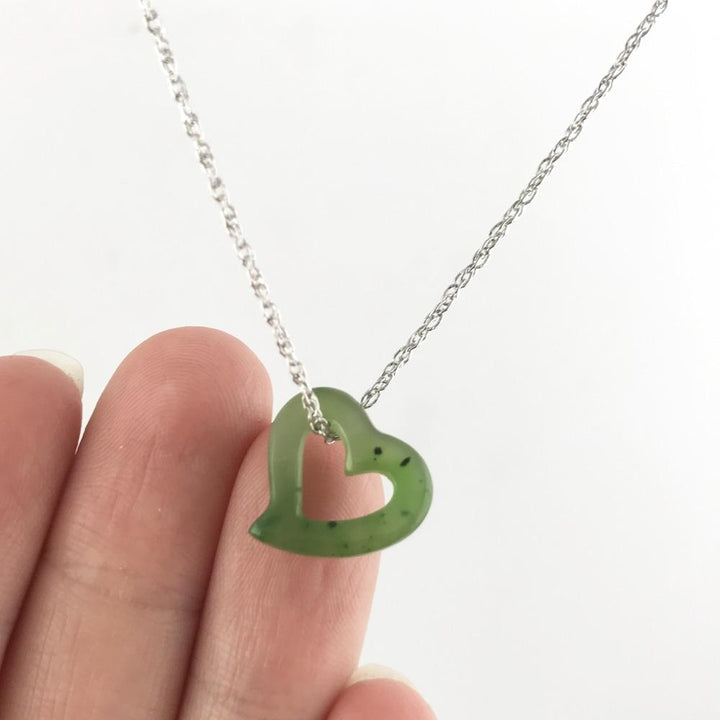 Green jade heart pendant with a hollow center held between fingers on a silver chain
