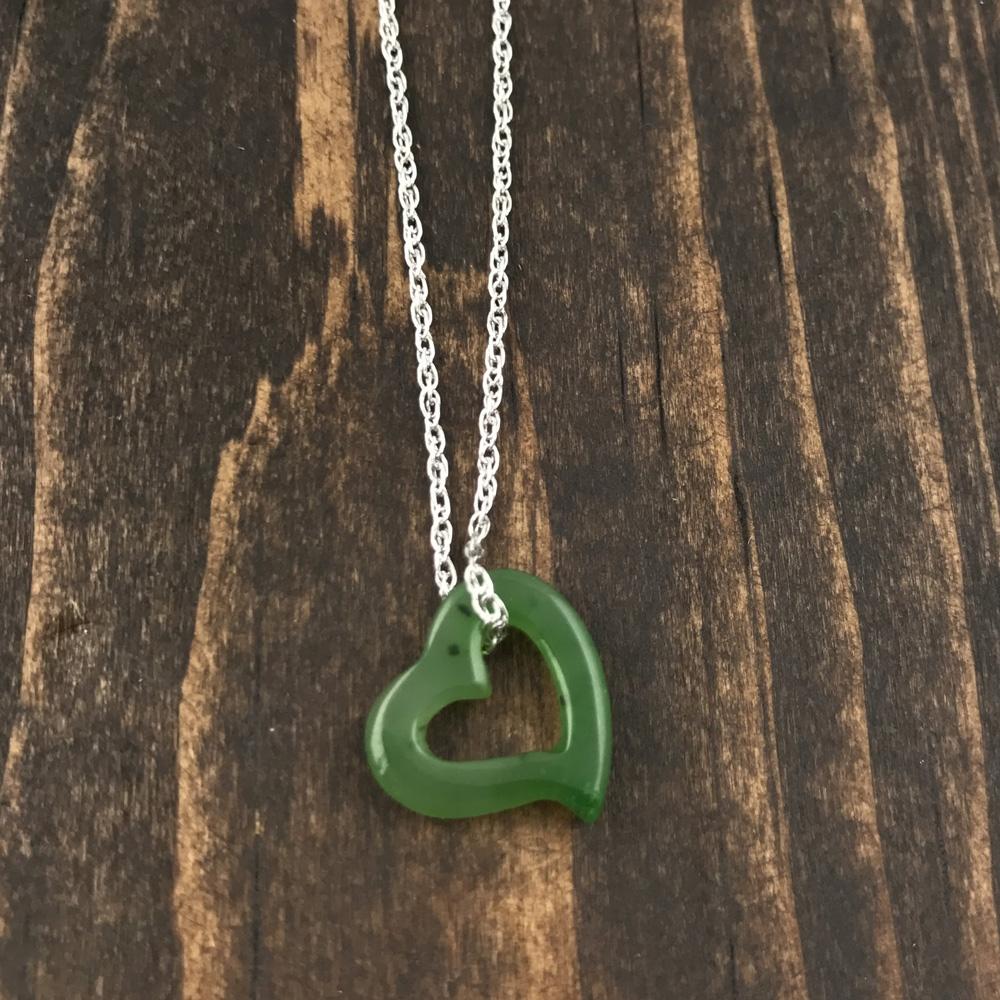 Green jade heart pendant with hollow center on a silver chain resting on dark wood surface