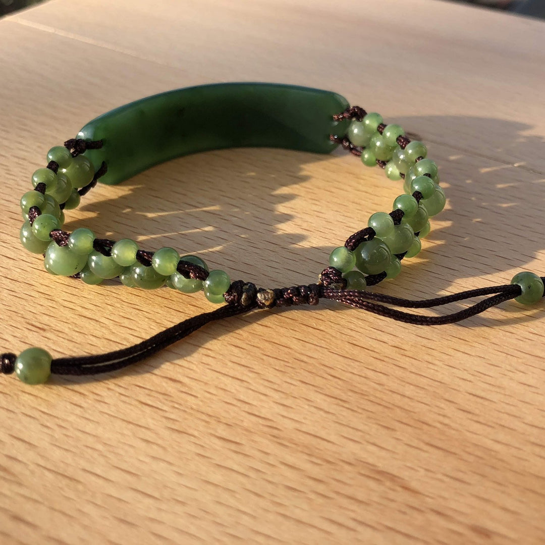 Green jade beaded wrap bracelet with adjustable black cord knots on a wooden surface