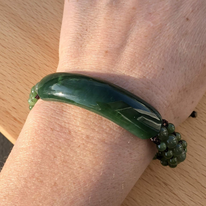 Green bracelet with a large curved central stone and multiple green bead accents worn on the wrist.