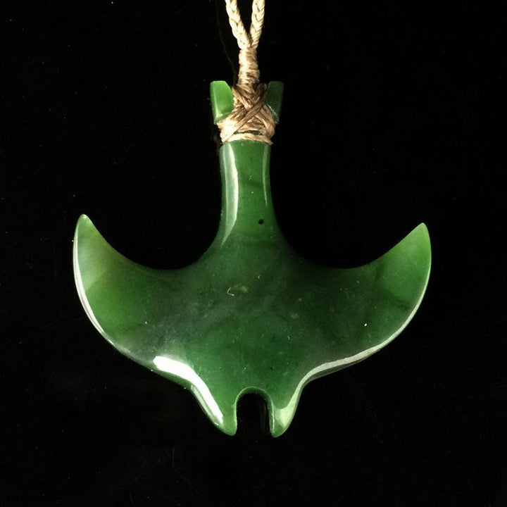 Green manta ray pendant suspended from a beige braided cord against a black background
