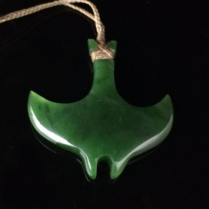 Green jade manta ray pendant suspended on a natural fiber cord against a black background